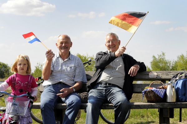 Herren auf einer Bank schwenken deutsch-niederländische Fahnen im Naturpark Moor-Veenland 
